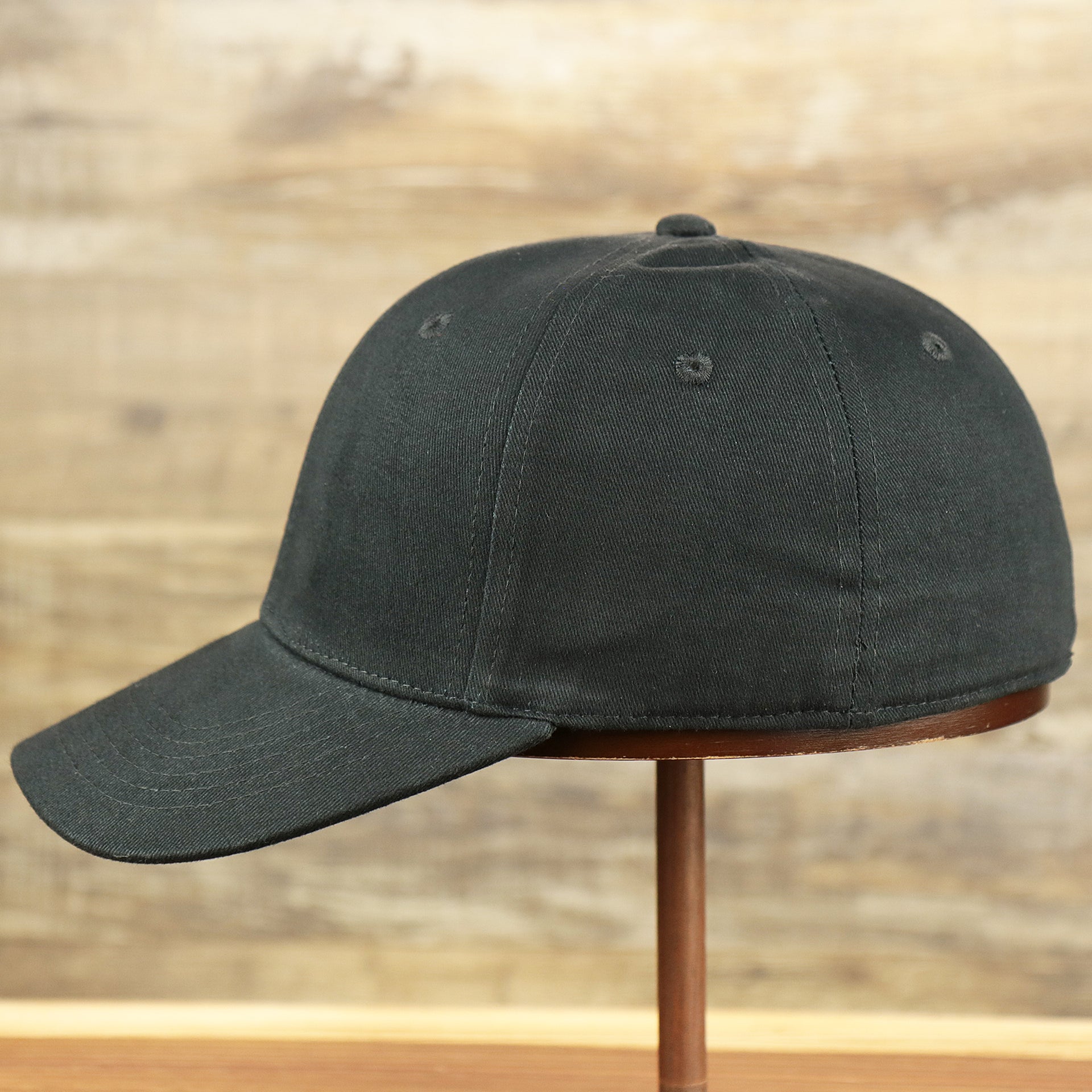 The wearer's left of the Jet Black Structured Cotton Blank Small Fit Flexfit Cap | Black Stretch Fit Caps