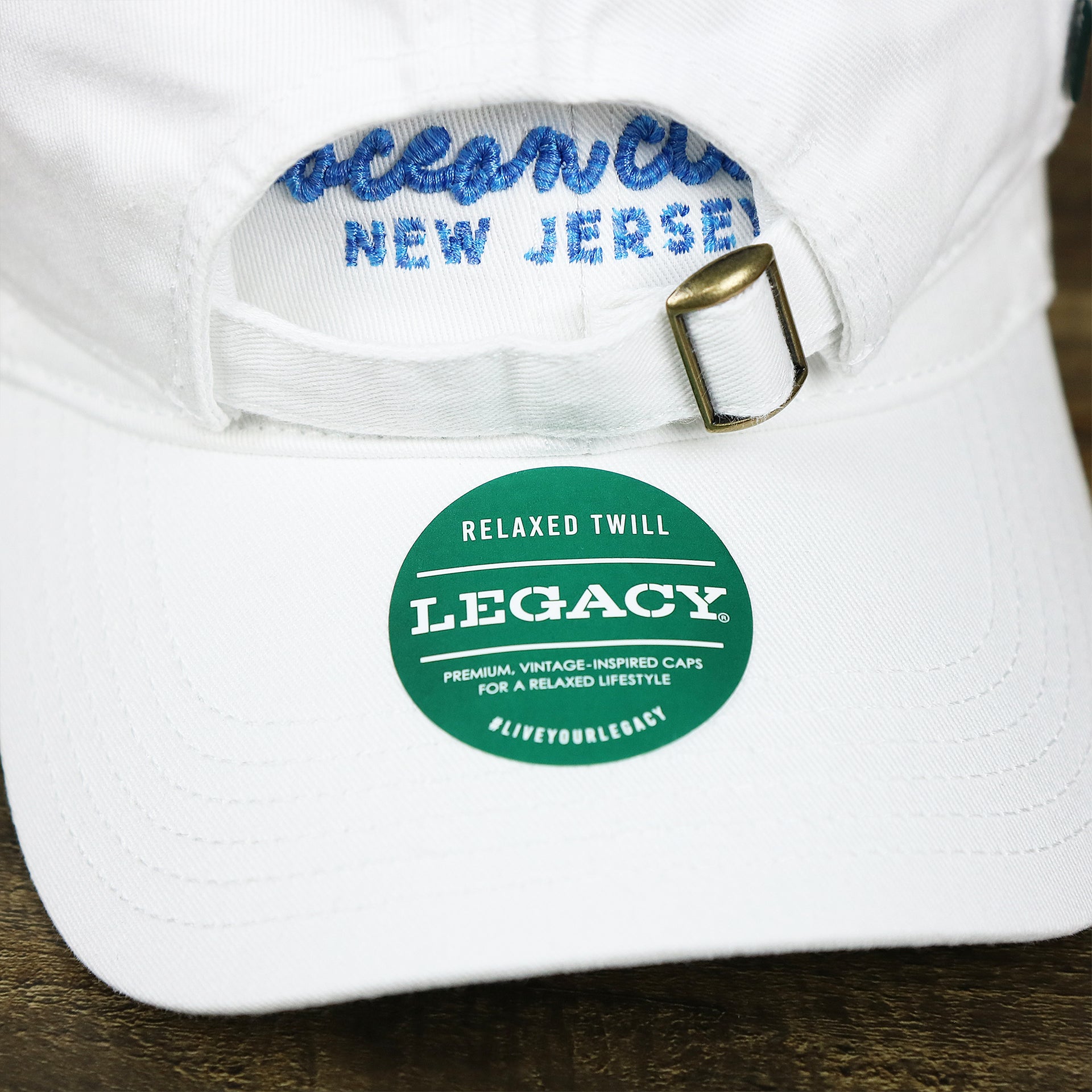 The Legacy Sticker on the OCNJ New Jersey Ocean City Cursive Wordmark Dad Hat | White Dad Hat 