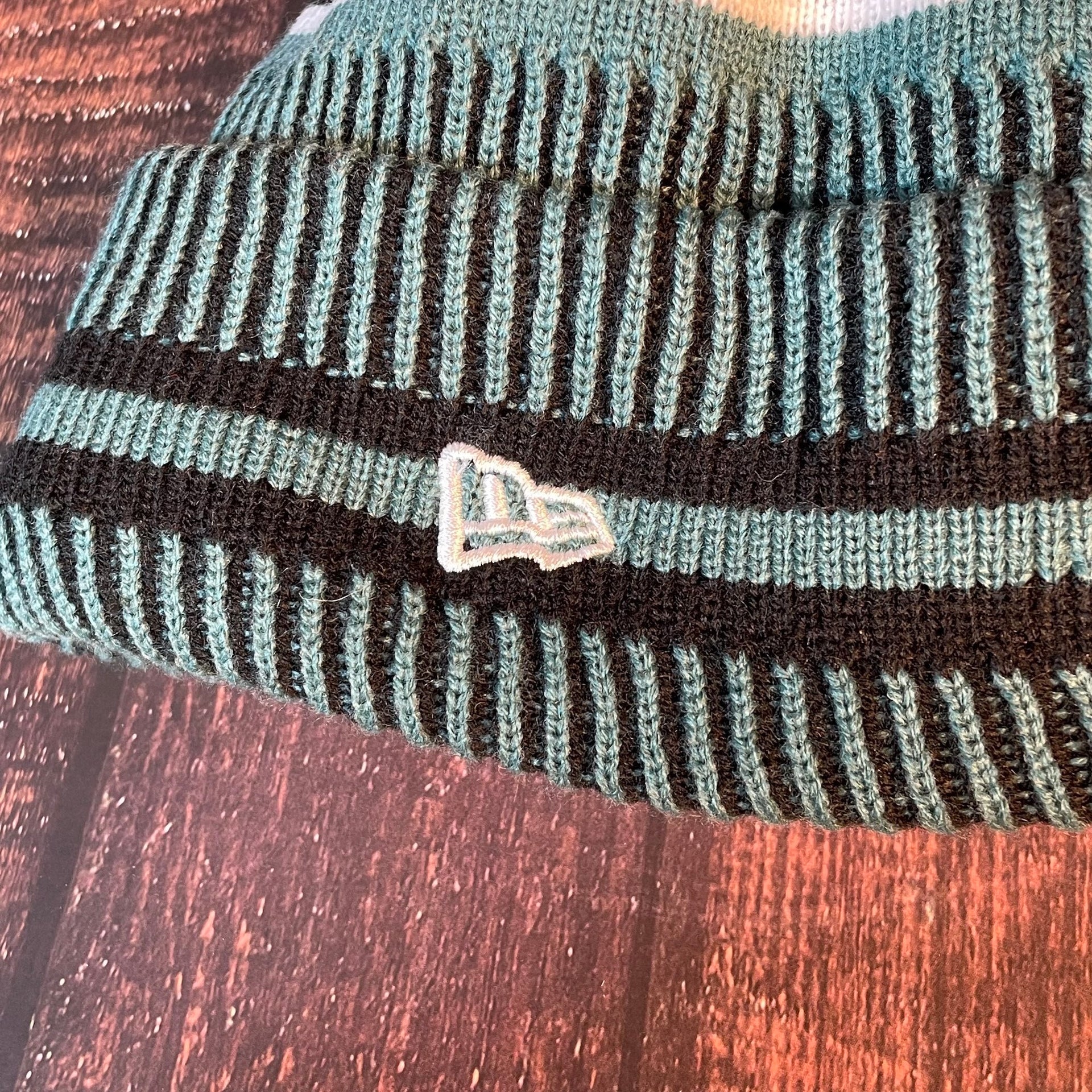Close up on the Philadelphia Eagles On Field Eagles Colorway Striped Pom Pom Beanie New Era Logo is white
