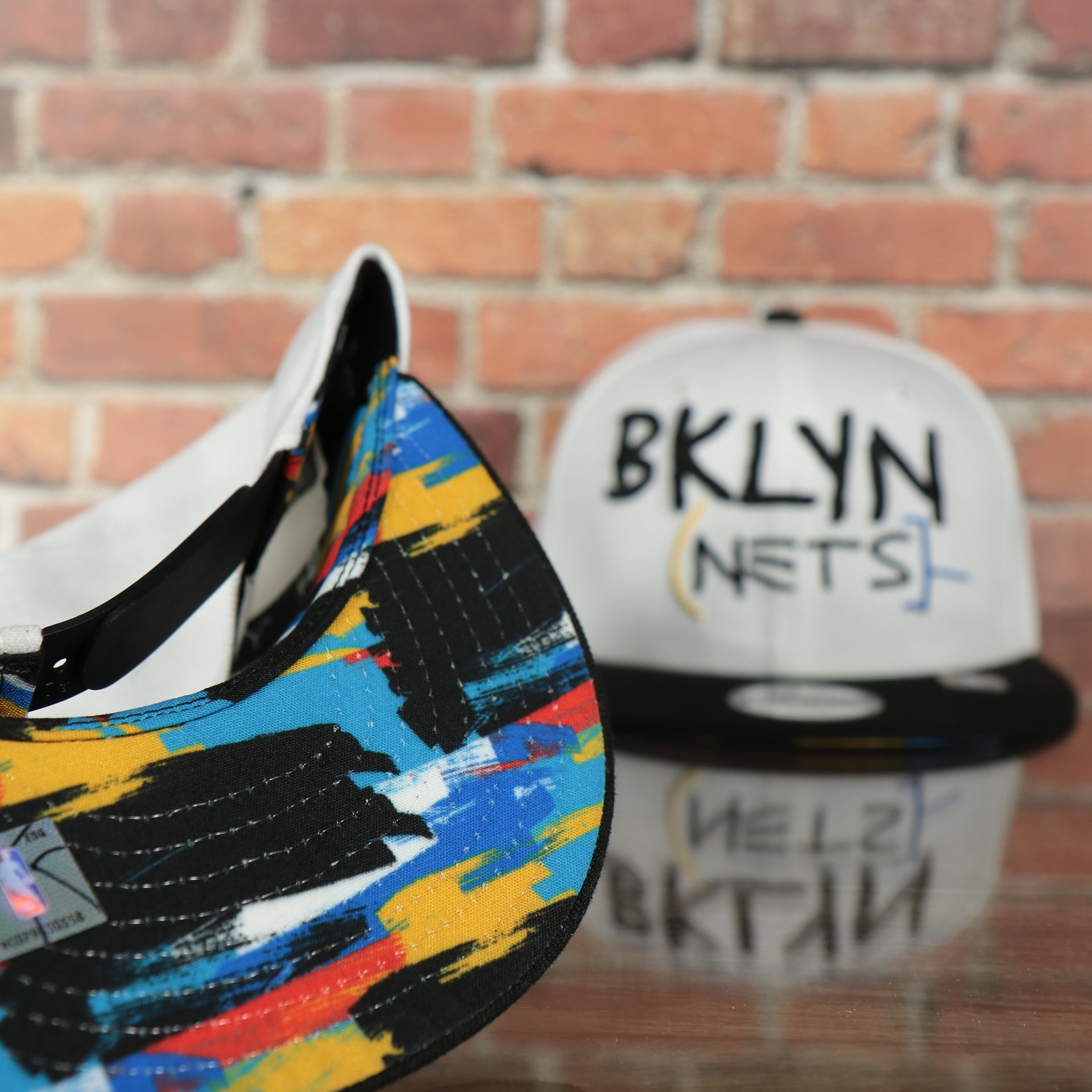 underside of the Brooklyn Nets 2022 City Edition BKLYN Nets Scribble Logo Multi-Color Bottom Youth 9Fifty Side Patch Snapback Cap | New Era, White