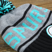 the Spurs Wordmark on the Retro San Antonio Spurs Striped Wordmark Cuffed Pom Pom Beanie | Gray And Black Winter Beanie