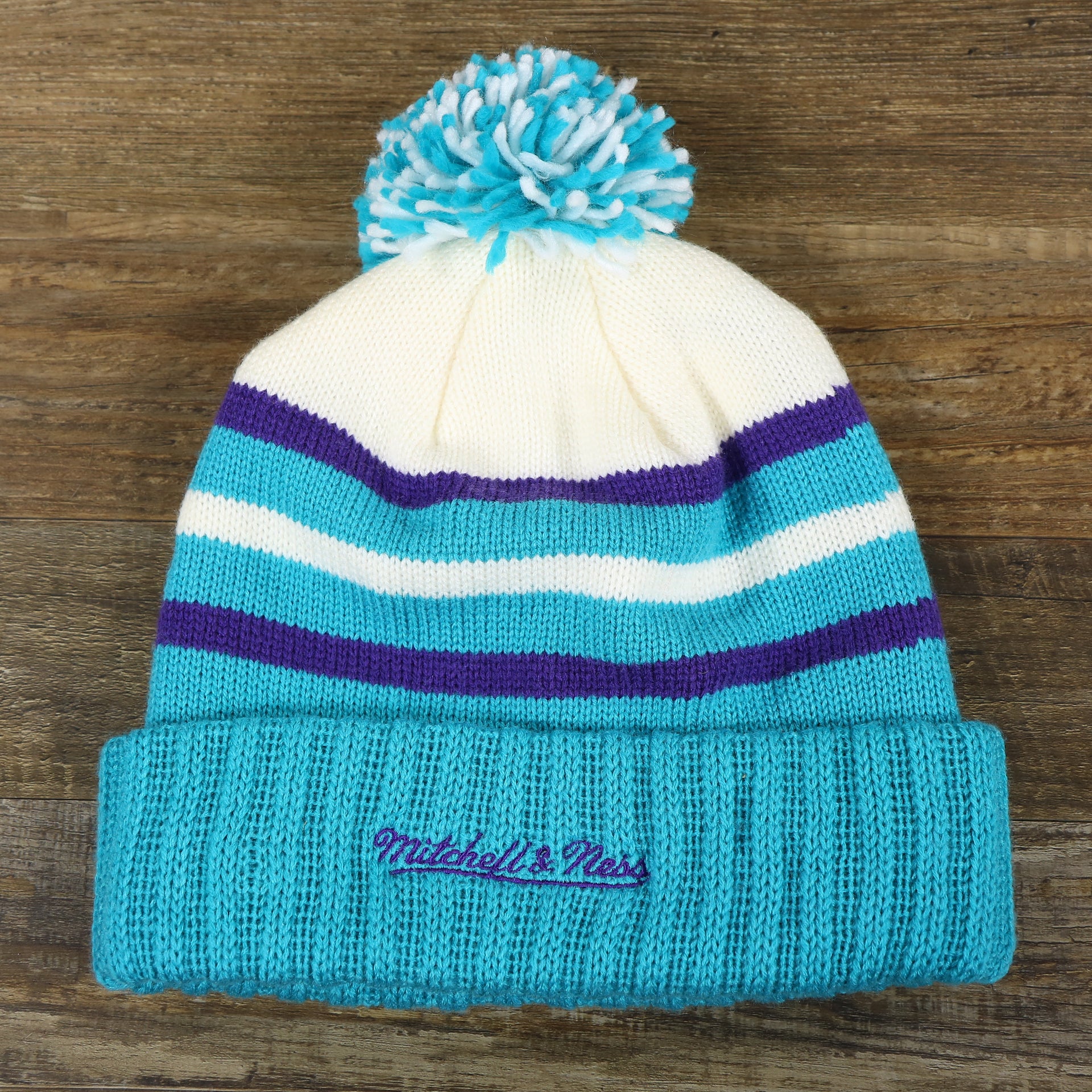 The backside of the Charlotte Hornets Cursive Wordmark Teal Blue Cuff Pom Pom Winter Beanie | Teal Blue Striped Winter Beanie