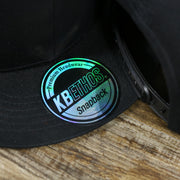 The KB Ethos Sticker on the Youth Jet Black Flat Brim Gray Bottom Blank Snapback Cap | Kid’s Black Snap Cap