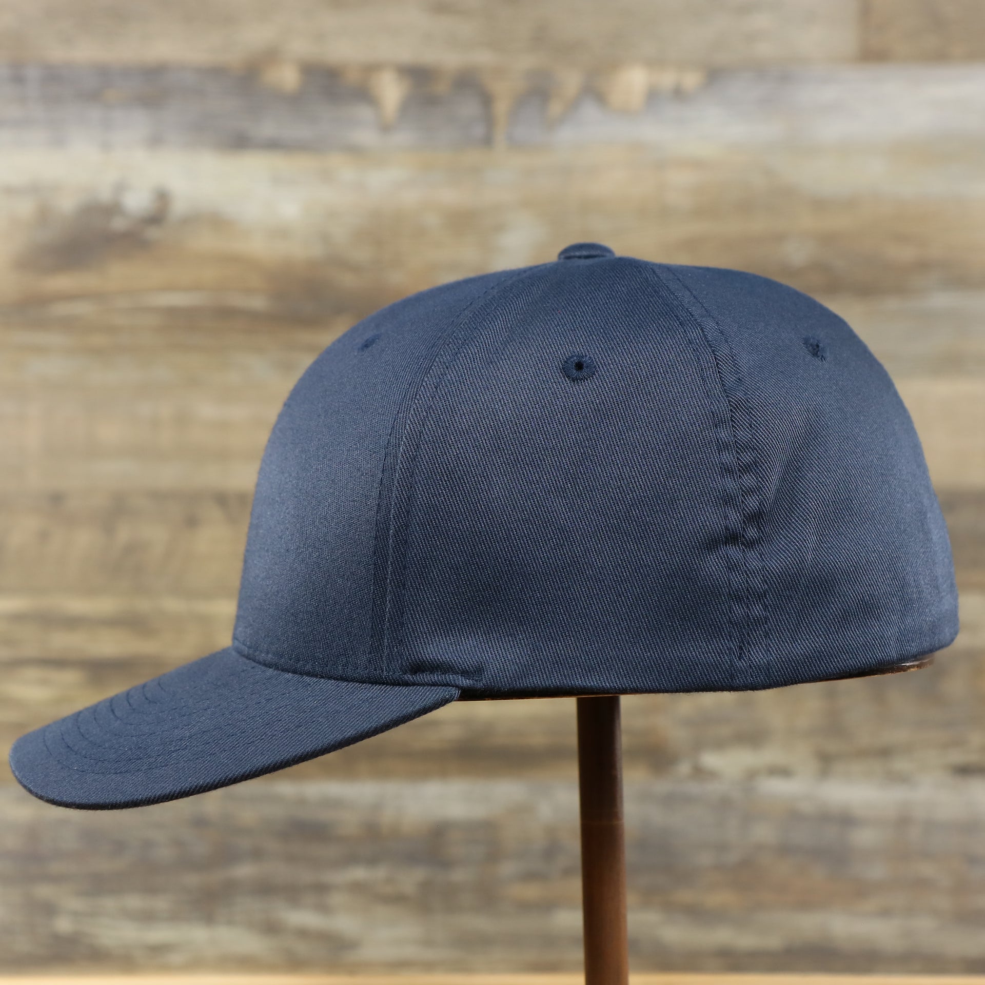 The wearer's left of the Jet Black Bent Brim Silver Bottom Blank FlexFit Cap | Black Flex Cap