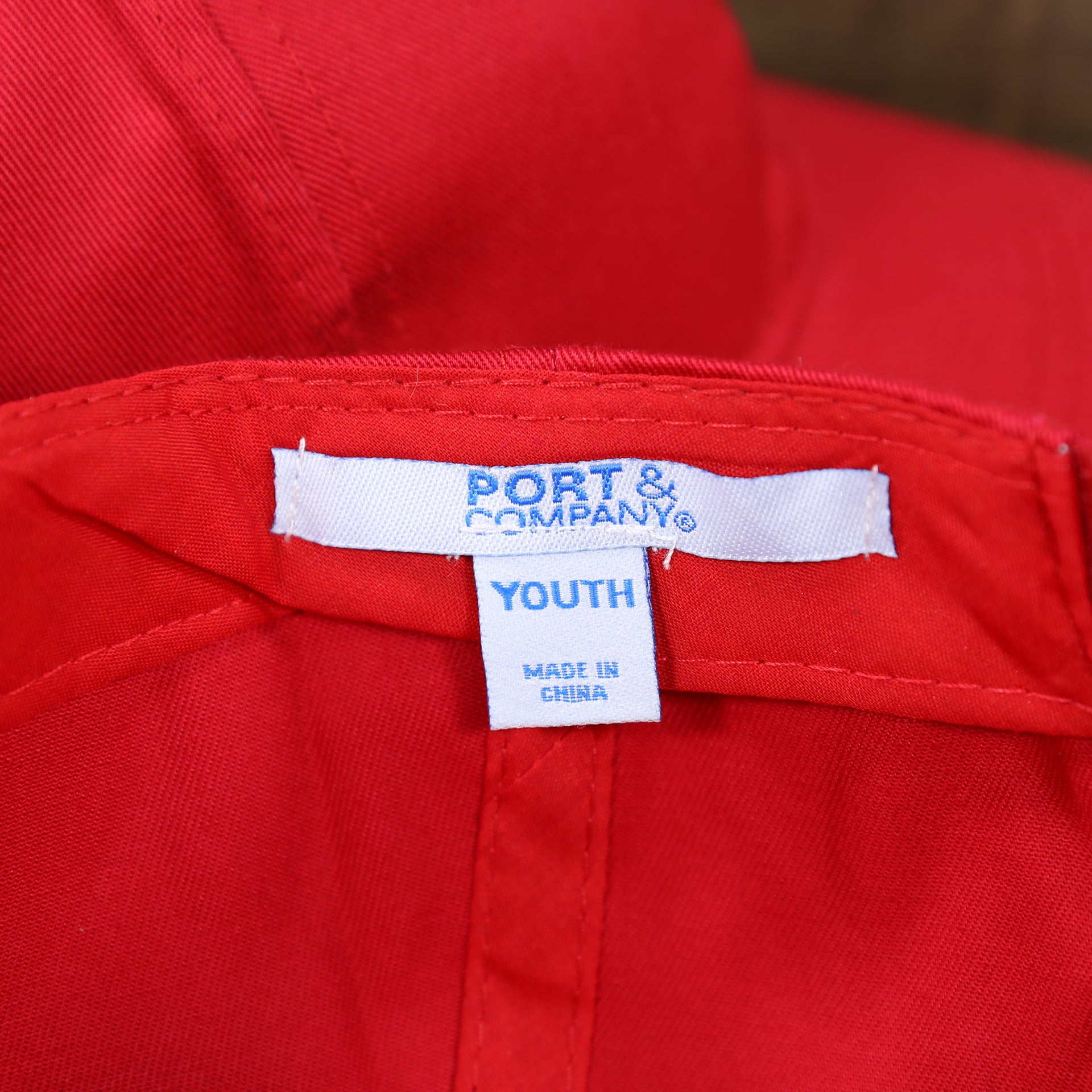 The Port and Company Tag on the Youth Cardinal Red Flat Brim Blank Baseball Hat | Kid’s Red Dad Hat