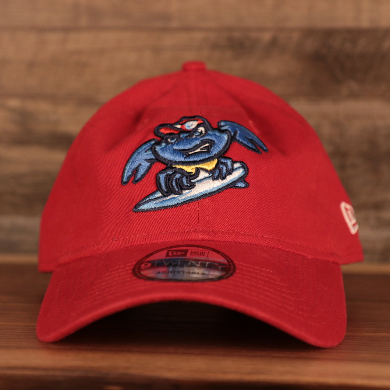 Embroidered on the front of the Jersey Shore BlueClaws baseball cap is the blue crab mascot for the BlueClaws. The logo is embroidered in light blue, yellow, white, and red, and features a blue crab riding a surf board.