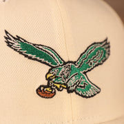 A close up of the green retro kelly logo on the front side of the cream Philadelphia Eagles 5950 fitted hat by New Era.