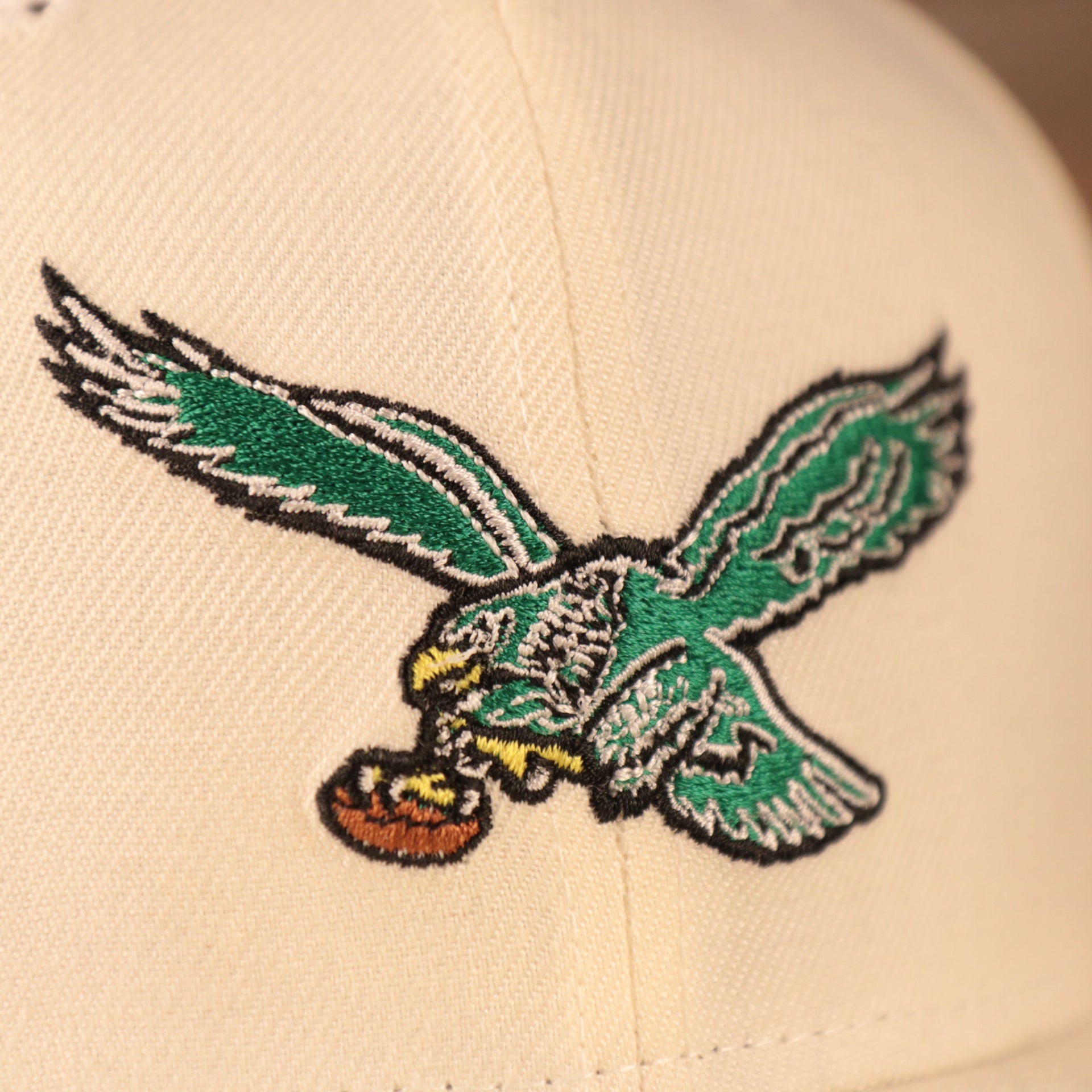 A close up of the green retro kelly logo on the front side of the cream Philadelphia Eagles 5950 fitted hat by New Era.
