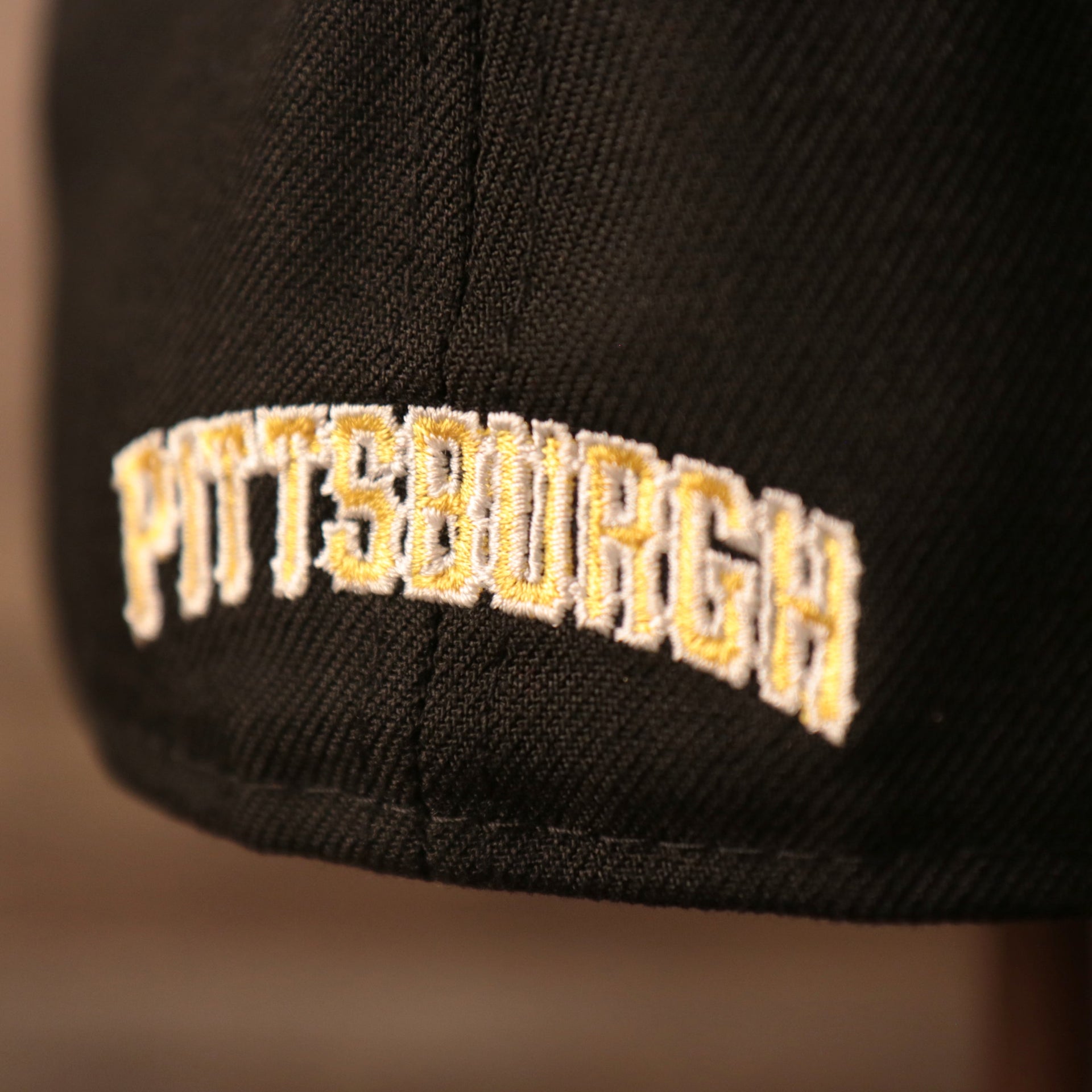 Pittsburgh written in old english arched font on the backside of the black 59fifty.