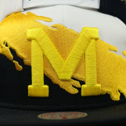 michigan logo on the University of Michigan Vintage Retro NCAA Paintbrush Mitchell and Ness Snapback Hat | Yellow/Navy Blue/White