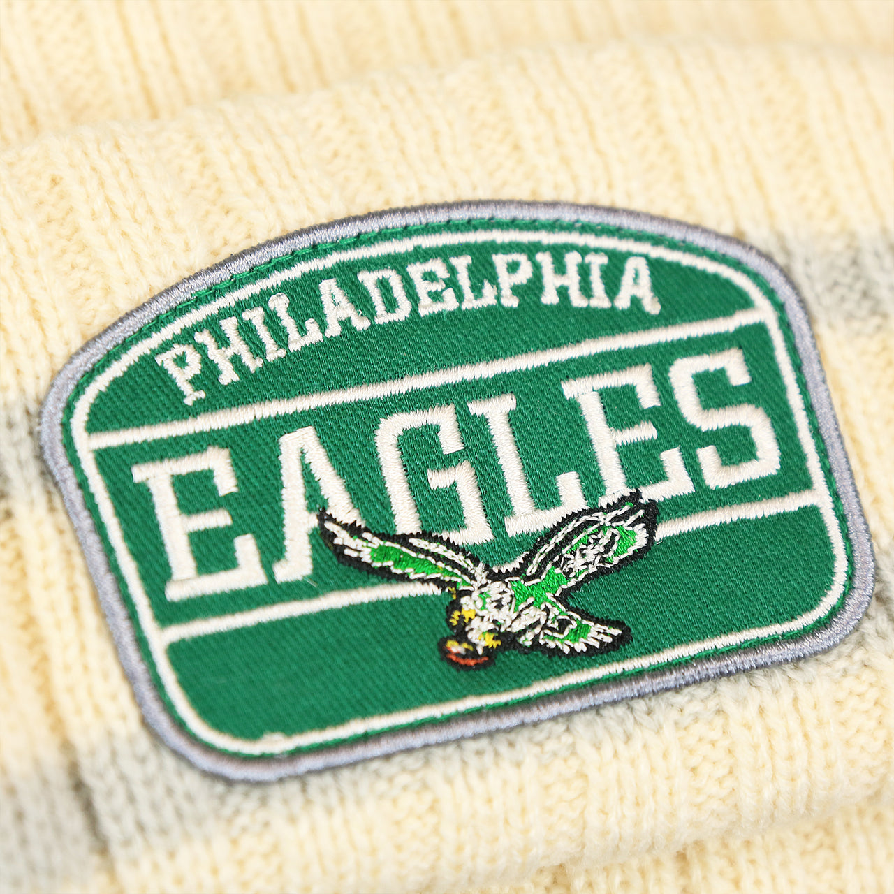 The Eagles Logo on the Throwback Philadelphia Eagles Legacy 1987 Eagles Patch Pom Pom Beanie | Natural Beanie