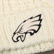 The Eagles Logo on the Women’s Philadelphia Eagles Cuffed Winter Knit Beanie With Meeko Pom Pom | Women’s Cream Winter Beanie