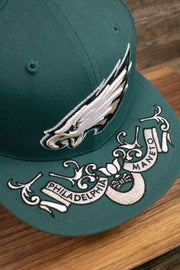 the top of the brim on the Philadelphia Eagles NFL Draft 2019 Snapback Hat | Philly Eagles Midnight Green 9Fifty Snapback Draft Hat has an Eagles slogan in Latin on it
