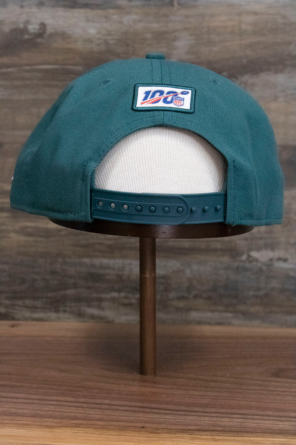 the back of the Philadelphia Eagles NFL Draft 2019 Snapback Hat | Philly Eagles Midnight Green 9Fifty Snapback Draft Hat has an NFL 100 patch and a plastic adjustable strap