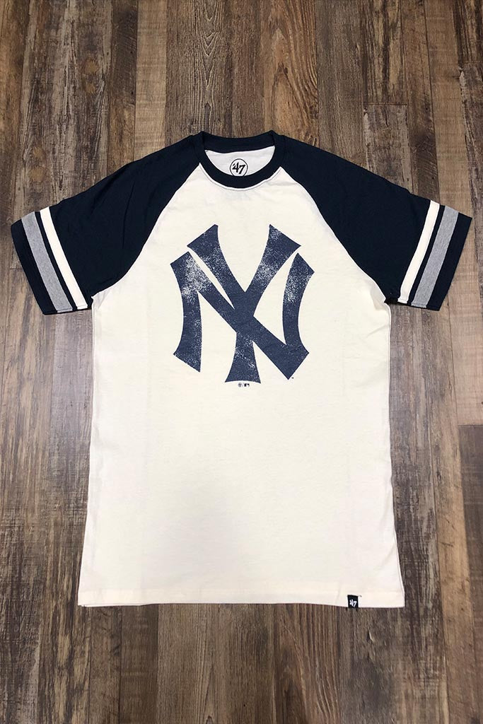 on the front of the New York Yankees Throwback Vintage 2-Tone T-Shirt | Distressed Yankees Logo Cooperstown Collection Heritage Opener Tee is a worn navy blue Yankees logo and pitcher stripe sleeves