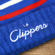 The LA Clippers Wordmark on the Los Angeles Clippers Cursive Wordmark Blue Cuff Pom Pom Winter Beanie | Blue Striped Winter Beanie