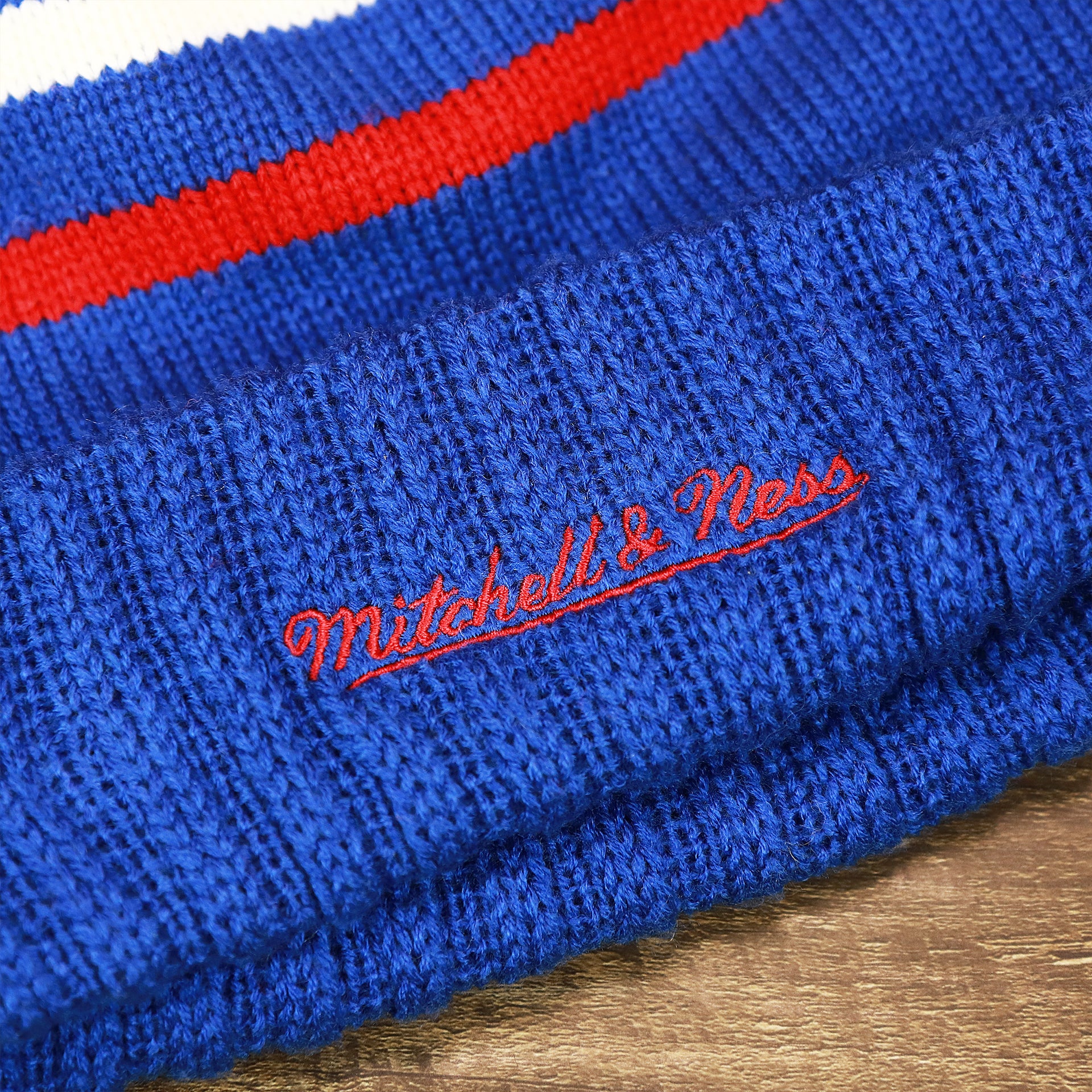 The Mitchell And Ness Script Logo on the Los Angeles Clippers Cursive Wordmark Blue Cuff Pom Pom Winter Beanie | Blue Striped Winter Beanie