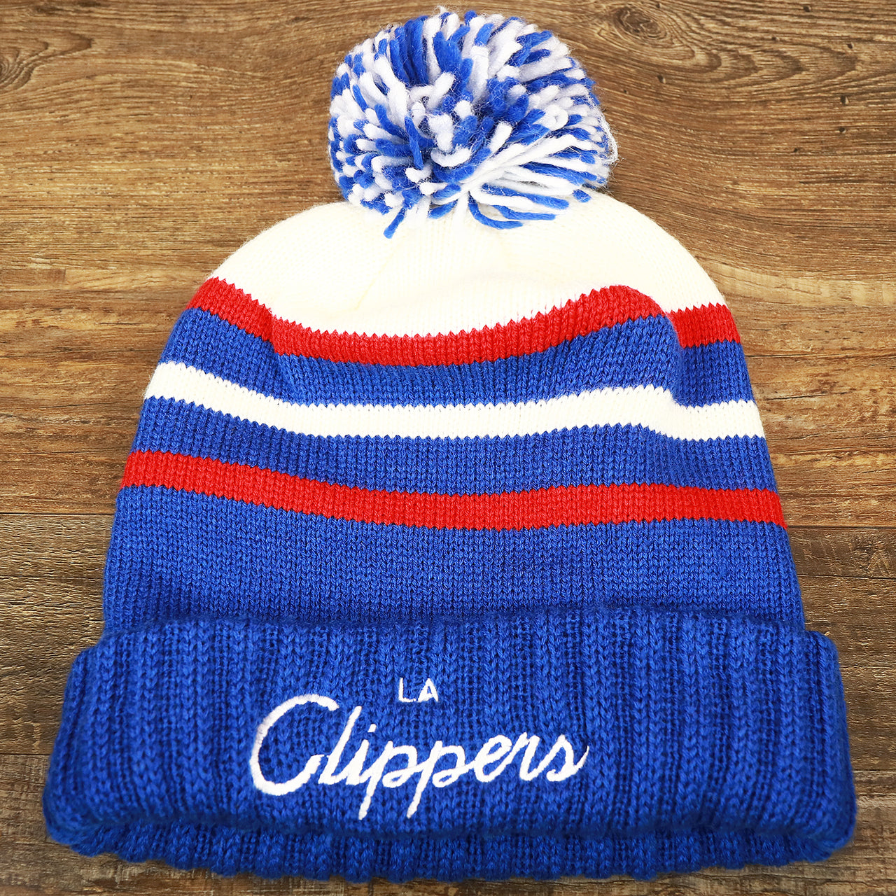 The front of the Los Angeles Clippers Cursive Wordmark Blue Cuff Pom Pom Winter Beanie | Blue Striped Winter Beanie