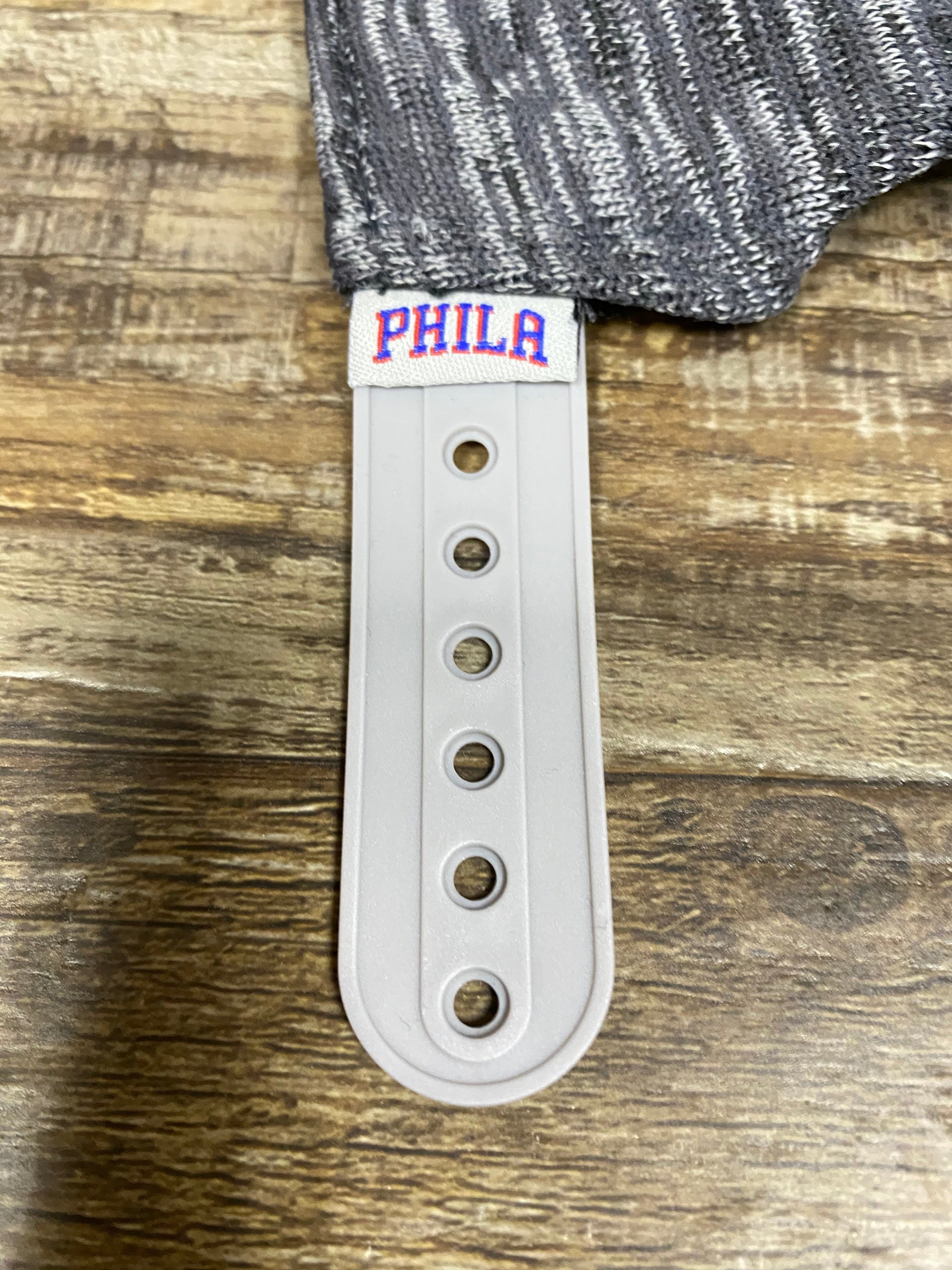 on the strap of the Philadelphia 76ers Flyknit Look Space Dye Gray Trucker Dad Hat is a Phila team logo tag