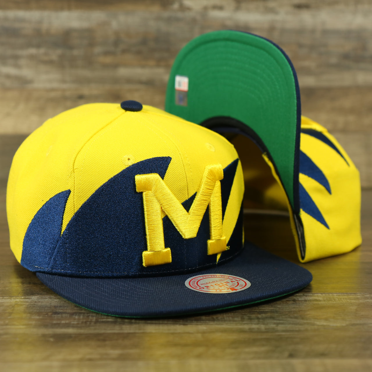 front and bottom of the University of Michigan Vintage Retro NCAA Sharktooth Mitchell and Ness Snapback Hat | Yellow/Navy Blue