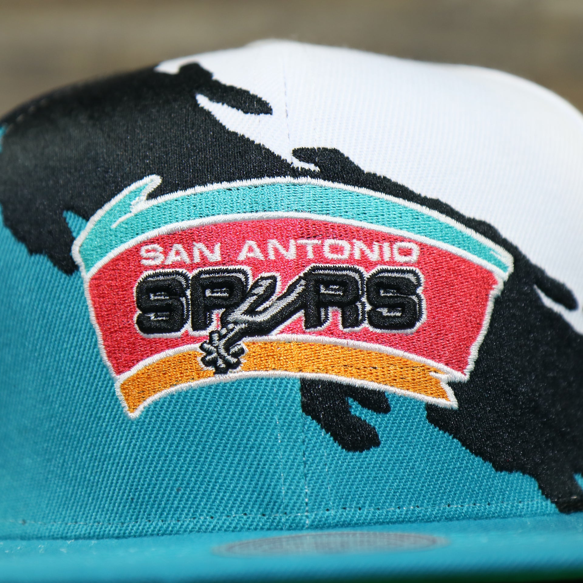 spurs logo on the San Antonio Spurs Vintage Retro NBA Paintbrush Mitchell and Ness Snapback Hat | Teal/White/Black