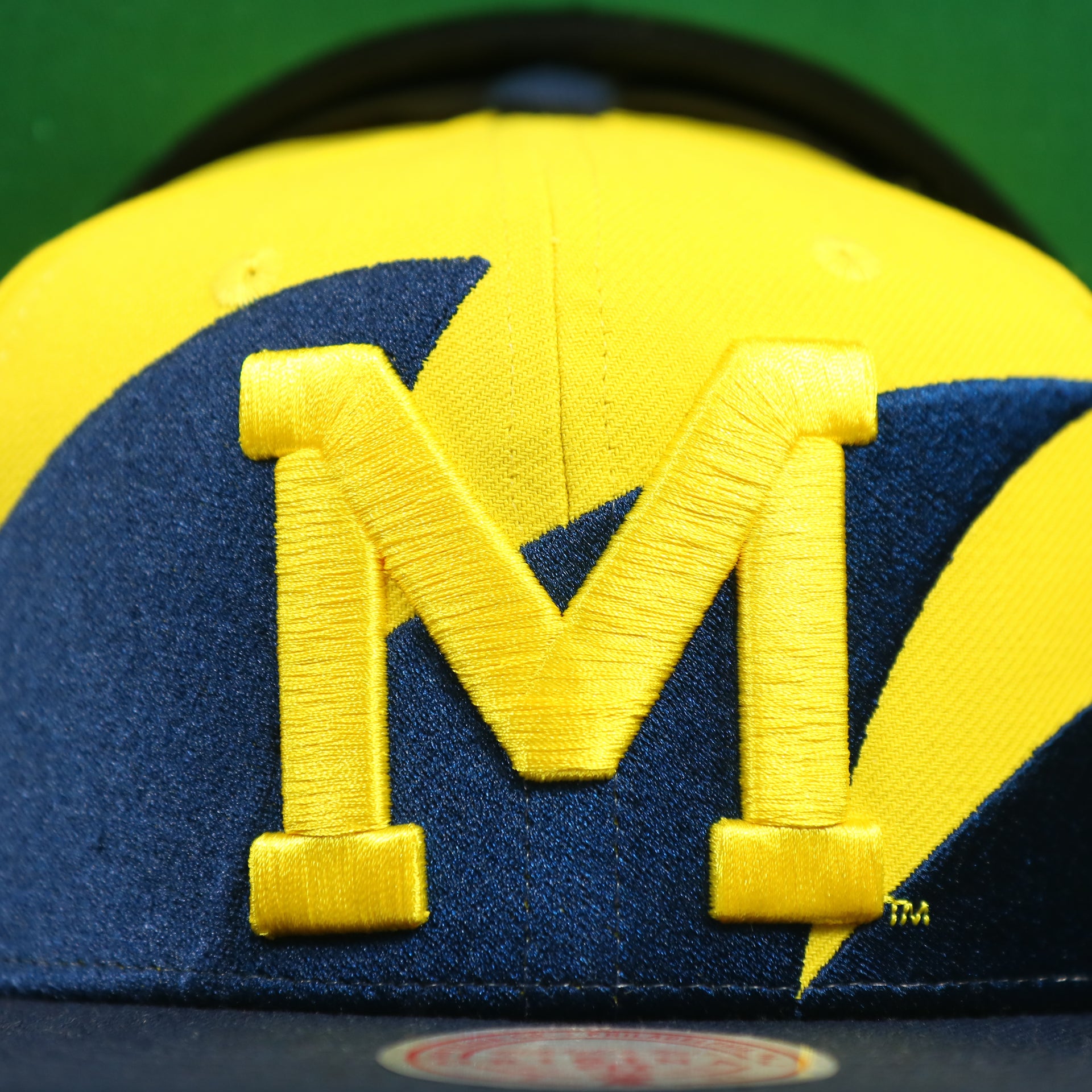 Michigan logo on the University of Michigan Vintage Retro NCAA Sharktooth Mitchell and Ness Snapback Hat | Yellow/Navy Blue