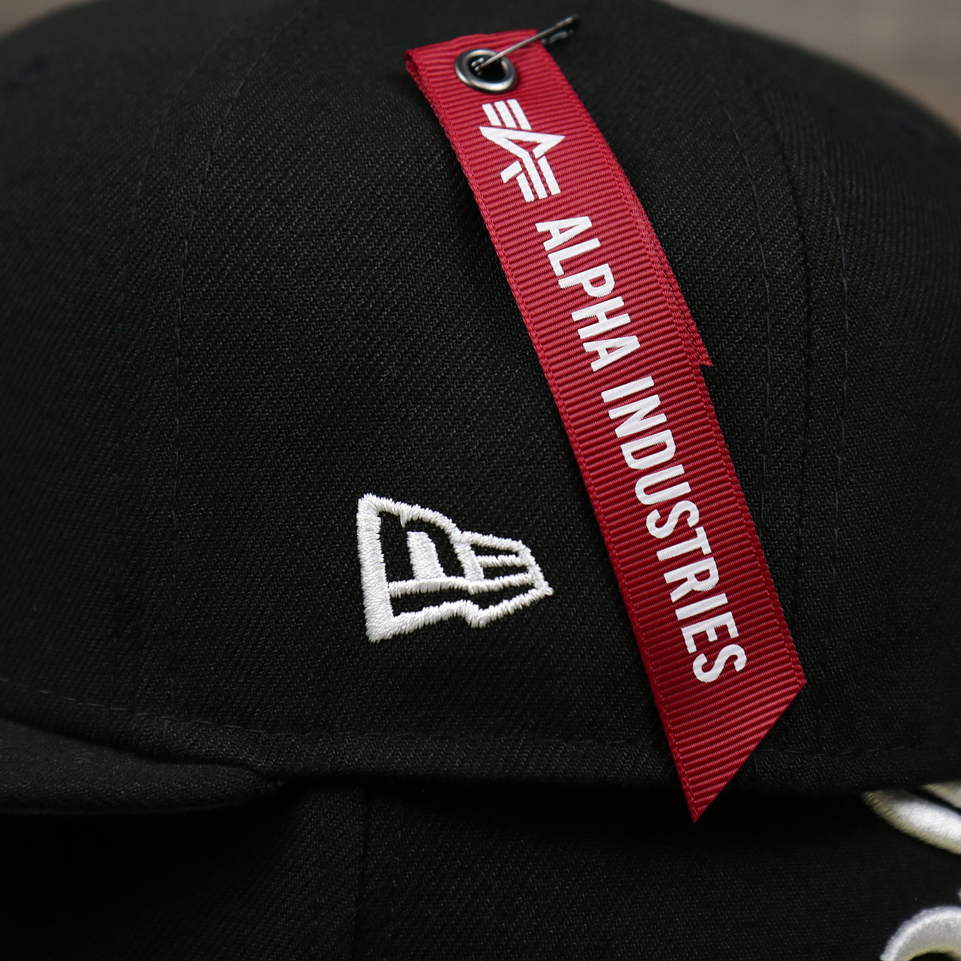 The New Era Logo on the Alpha Industries Hangtag on the Chicago White Sox Alpha Industries Side Patch Army Green Undervisor 59FIfty Fitted Cap With Hangtag | Black 59FIfty Cap