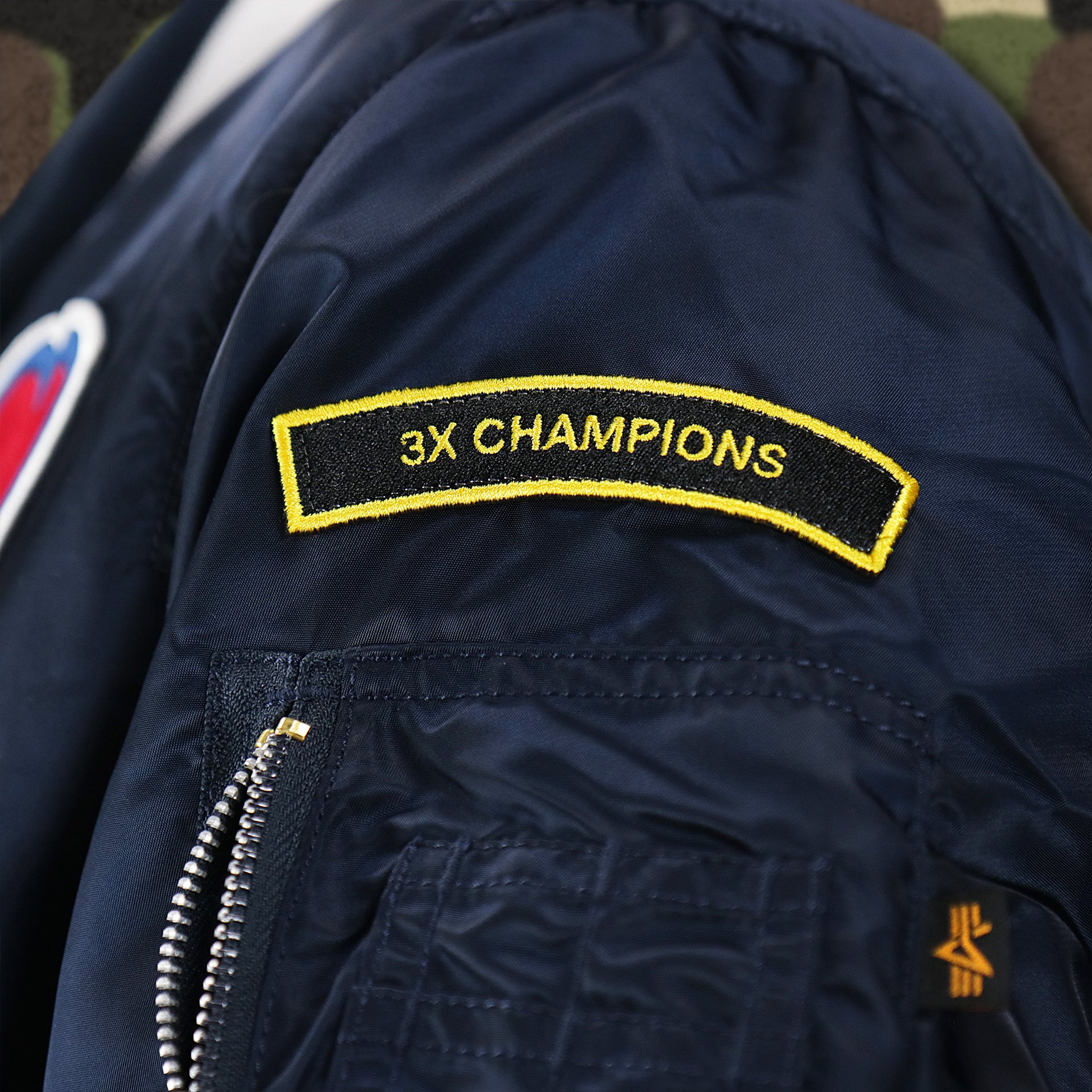 The 3x Champions Side Patch on the Atlanta Braves MLB Patch Alpha Industries Reversible Bomber Jacket With Camo Liner | Navy Blue Bomber Jacket