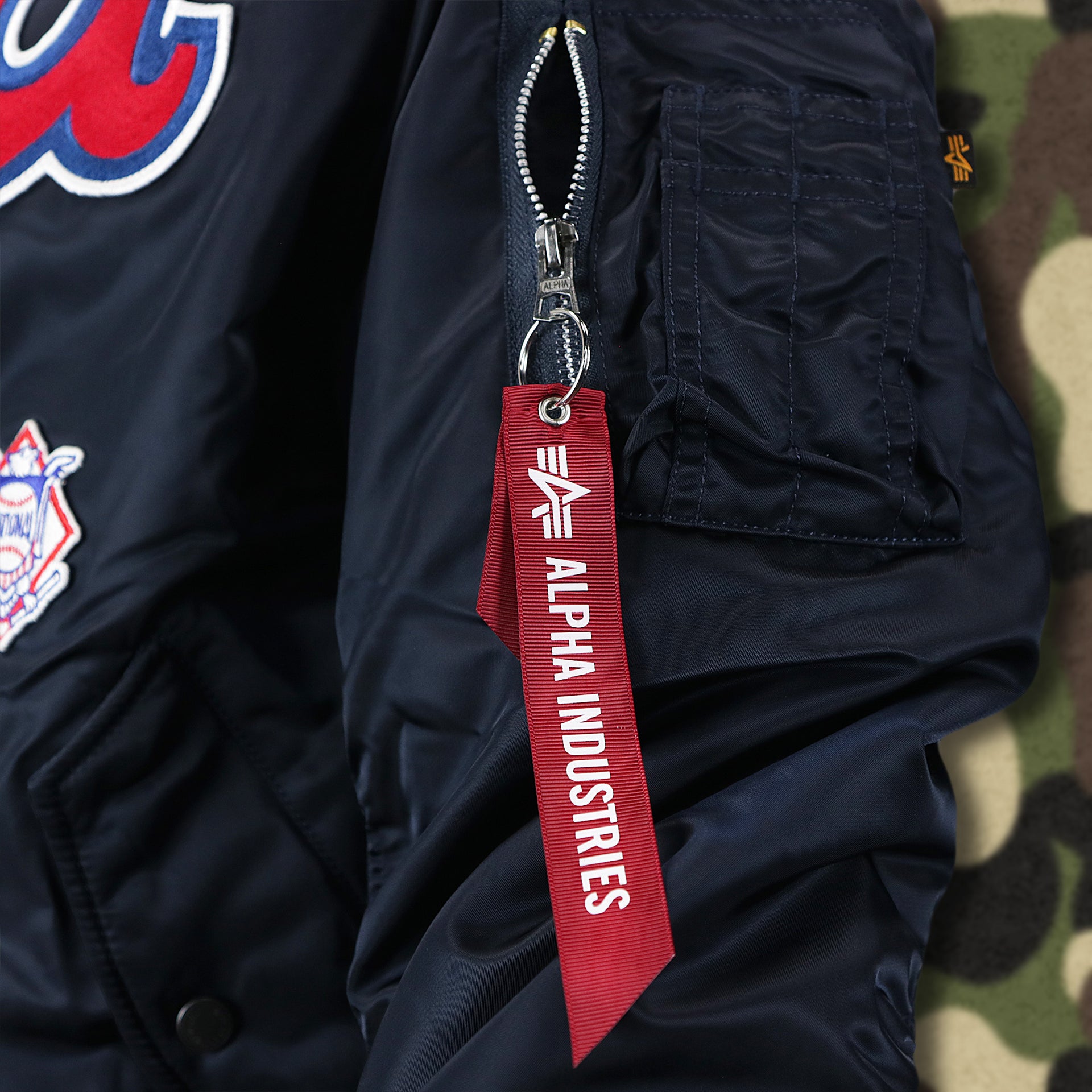 The Alpha Industries Hangtag on the Atlanta Braves MLB Patch Alpha Industries Reversible Bomber Jacket With Camo Liner | Navy Blue Bomber Jacket