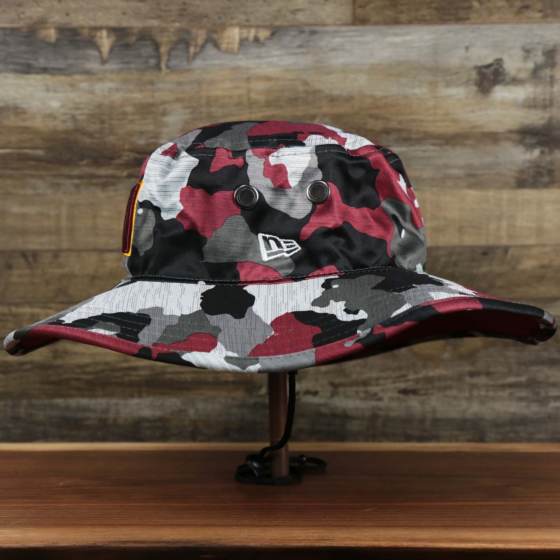 The wearer's left on the Washington Commanders NFL Summer Training Camp 2022 Camo Bucket Hat | Burgundy Bucket Hat