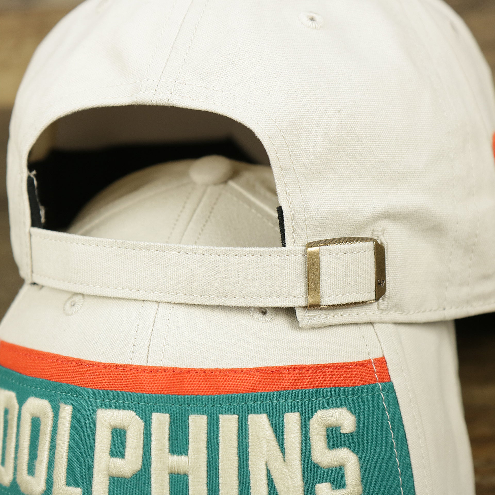 The adjustable strap on the Throwback Miami Dolphins Striped Wordmark Legacy Dolphins Side Patch Crossroad Dad Hat | Bone Dad Hat