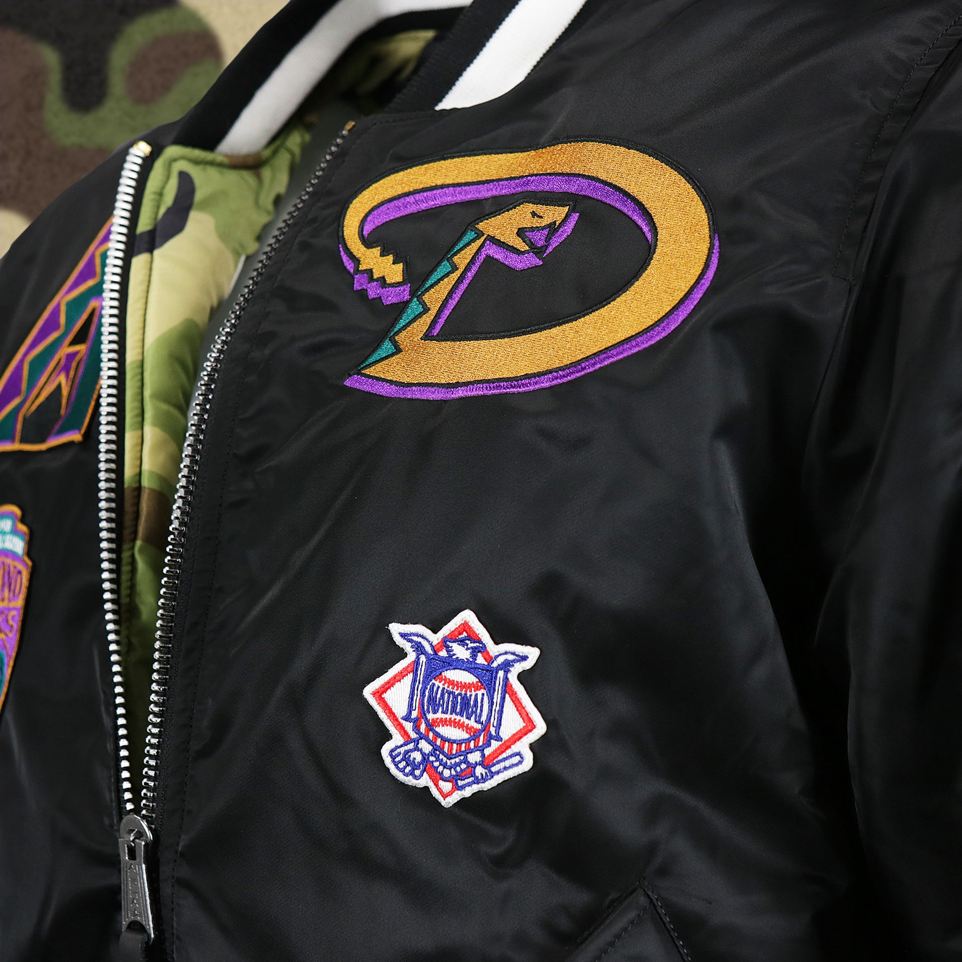 The Retro Diamondbacks Snake Logo Patch and the National Baseball Side Patch on the Cooperstown Arizona Diamondbacks MLB Patch Alpha Industries Reversible Bomber Jacket With Camo Liner | Black Bomber Jacket