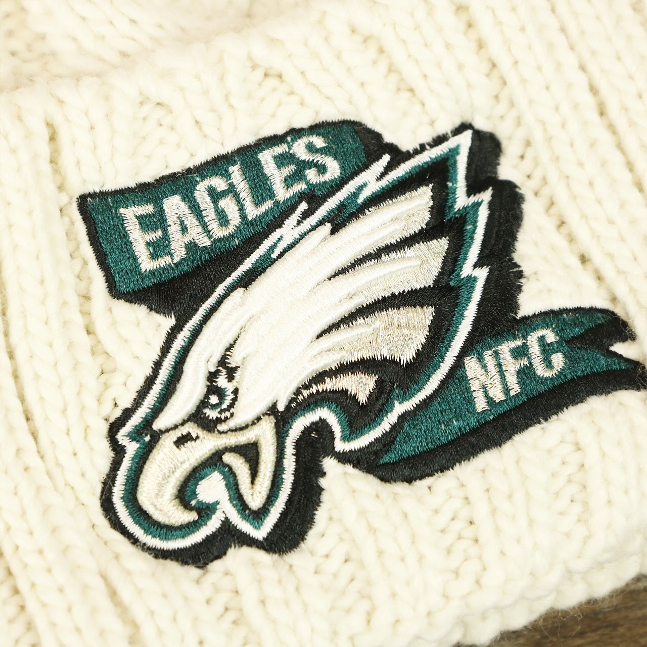 The Eagles NFC Logo on the Women’s Philadelphia Eagles 2022 NFC Cuffed Winter Knit Meeko Pom Pom Beanie | Women’s White Winter Beanies