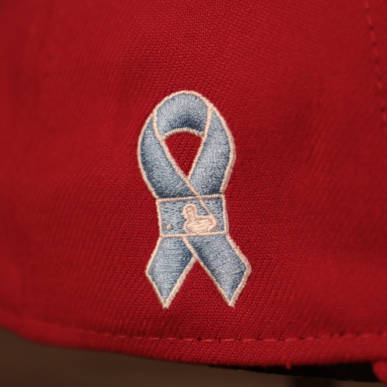 A close up of the light blue ribbon patch on the wearer's right side of the Philadelphia Phillies red fathers day 2021 39thirty flexfit cap by New Era.