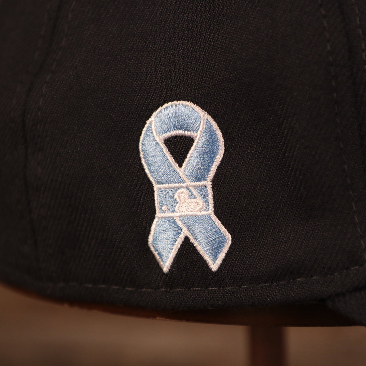A close up shot of the light blue ribbon patch on the wearer's right side of the navy blue Yanks fathers day 2021 39thirty flexfit cap by New Era.