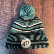 The front of the Philadelphia Eagles On Field Eagles Colorway Striped Pom Pom Beanie features Eagles logo