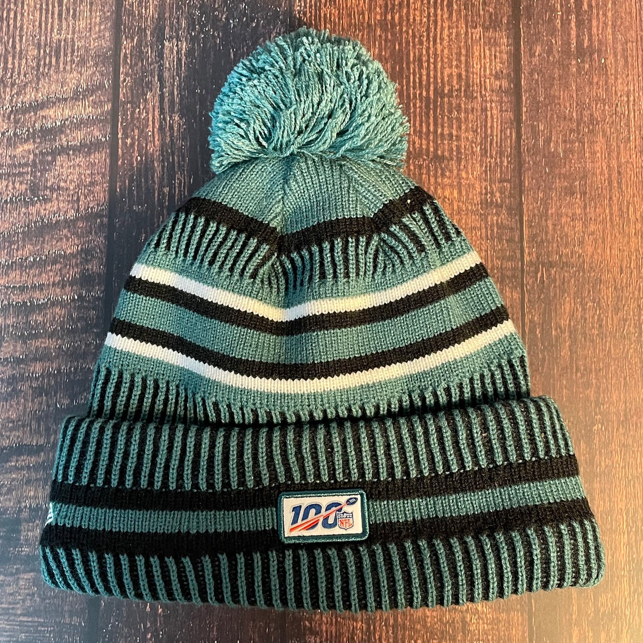 The back of the Philadelphia Eagles On Field Eagles Colorway Striped Pom Pom Beanie features the NFL logo