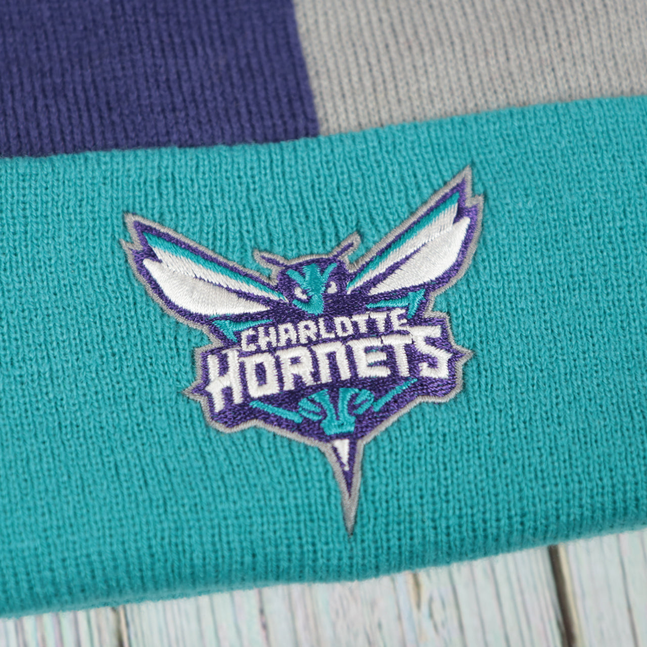 hornets logo on the Charlotte Hornets Cuffed Logo Split Beanie With Black Pom Pom | Teal, White, And Black Beanie