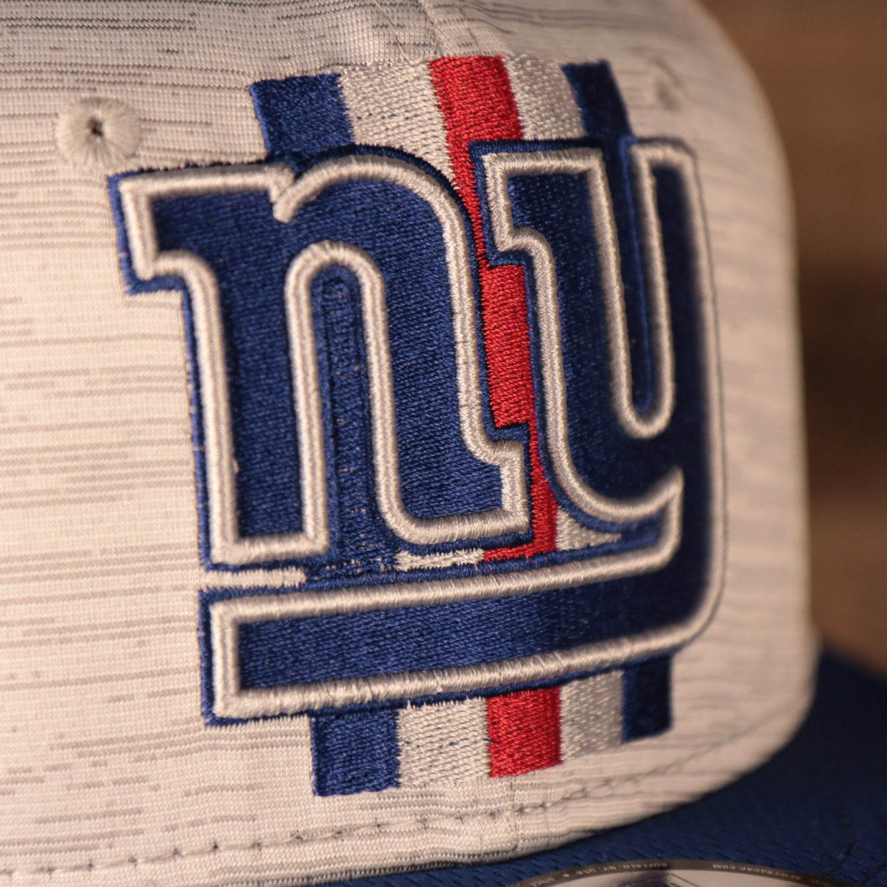 A closeup shot of the New York Giants patch on the front of the new era training 2021 gray snapback hat.