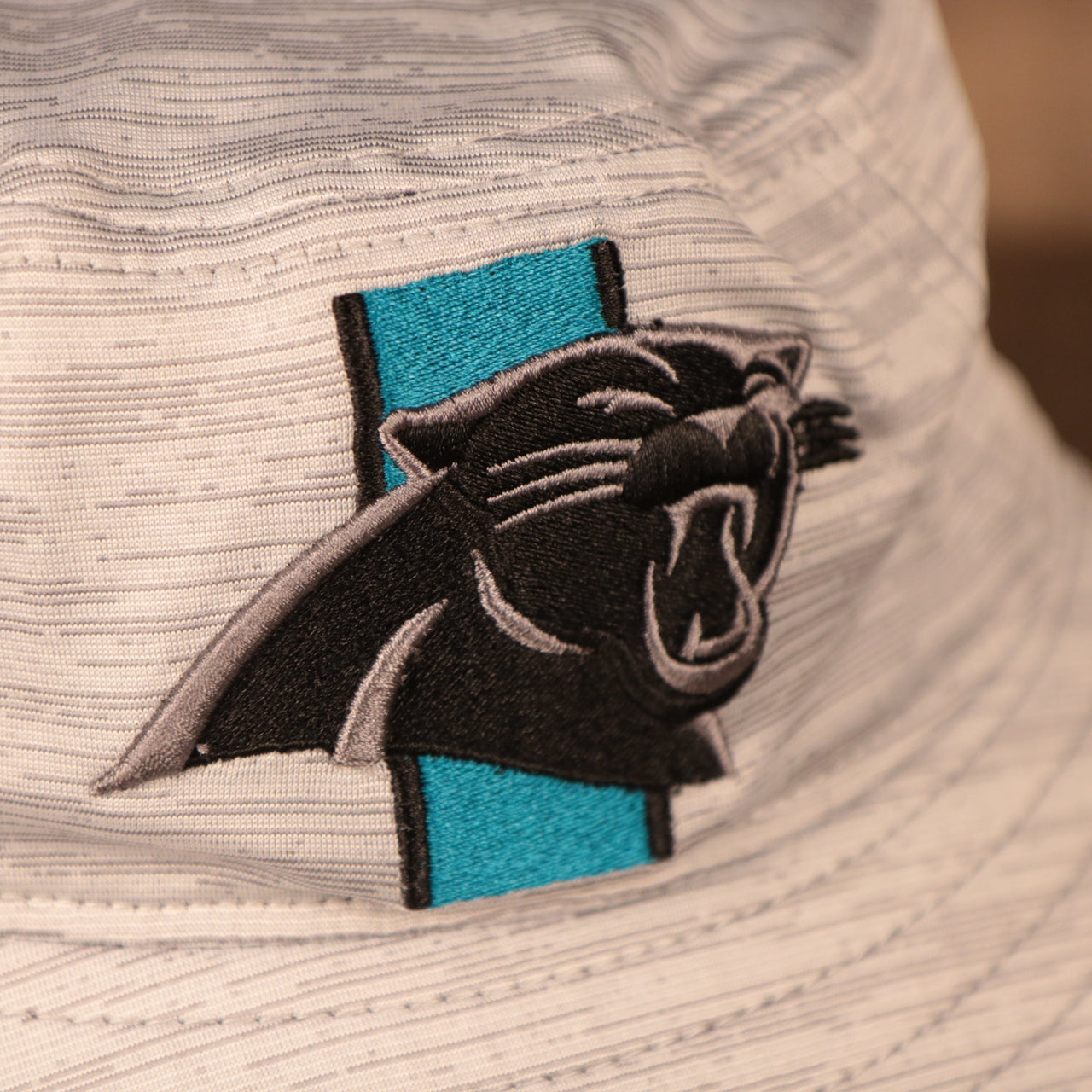 A closeup shot of the Carolina Panthers patch of the gray nfl on field training bucket hat by New Era.