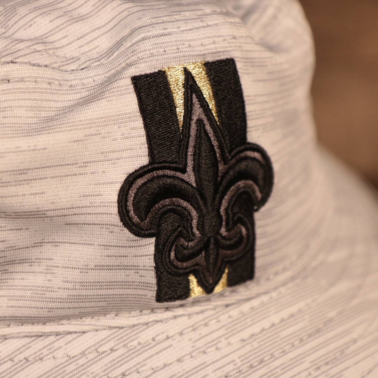 A closeup shot of the New Orleans Saints patch of the gray nfl on field training bucket hat by New Era.