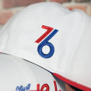76ers vintage logo on the wearers right side of the Philadelphia 76ers 2022 City Edition City Of Brotherly Love Blue Bottom 59Fifty Side Patch Fitted Cap | New Era, White