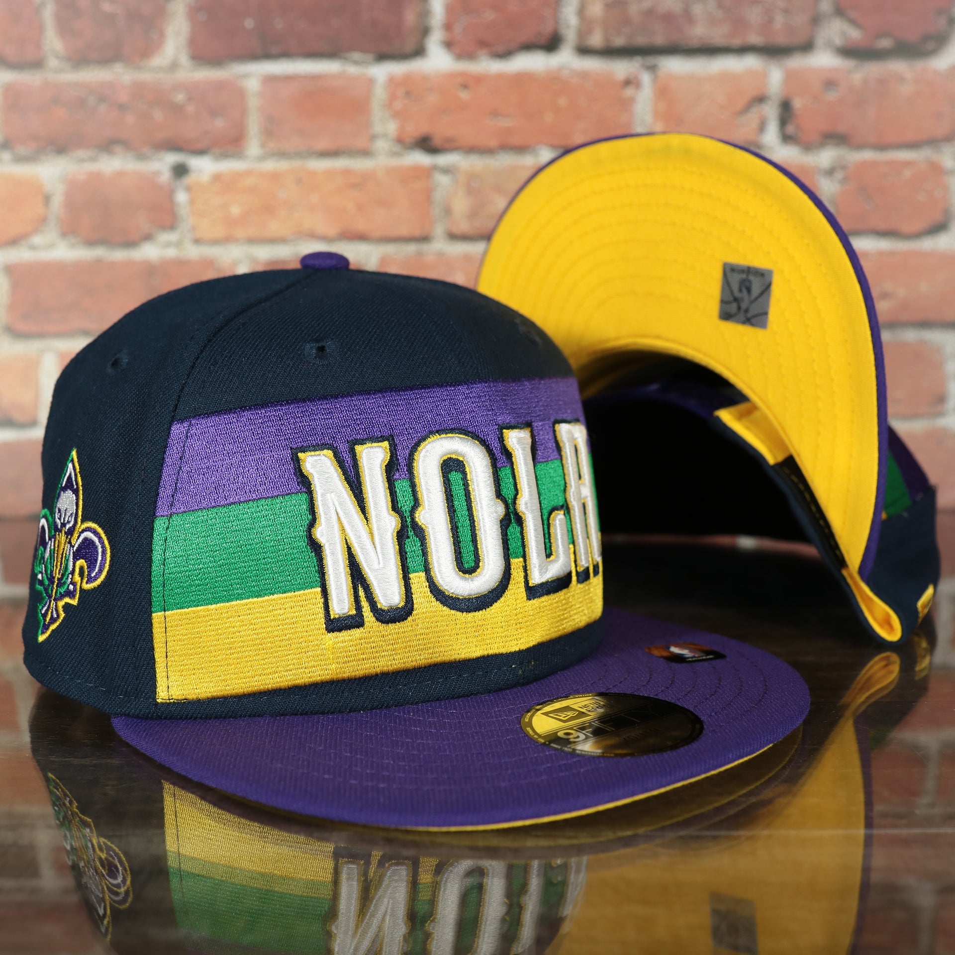 front and bottom of the New Orleans Pelicans 2022 City Edition NOLA Logo Yellow Bottom Youth 9Fifty Side Patch Snapback Cap | New Era, Navy