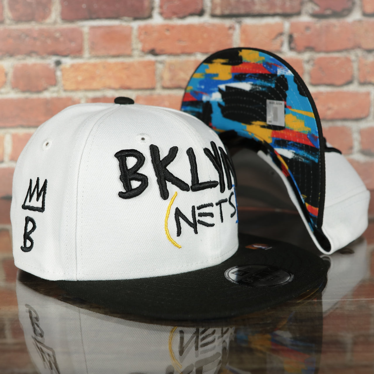 front and bottom of the Brooklyn Nets 2022 City Edition BKLYN Nets Scribble Logo Multi-Color Bottom Youth 9Fifty Side Patch Snapback Cap | New Era, White