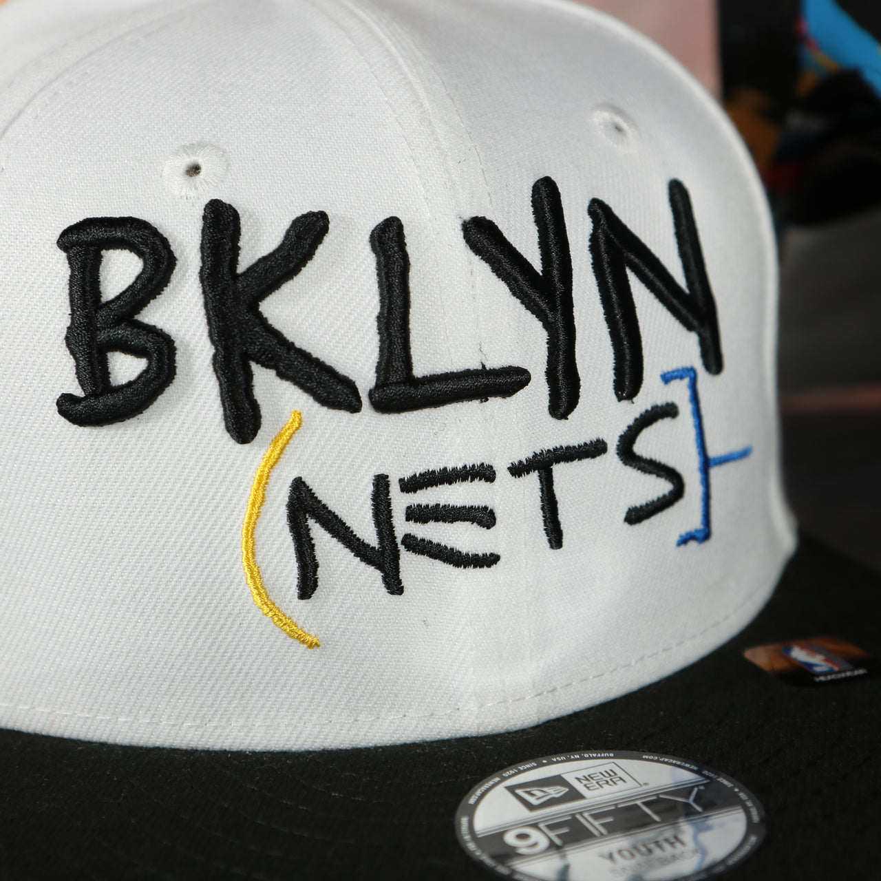 front logo on the front side of the Brooklyn Nets 2022 City Edition BKLYN Nets Scribble Logo Multi-Color Bottom Youth 9Fifty Side Patch Snapback Cap | New Era, White