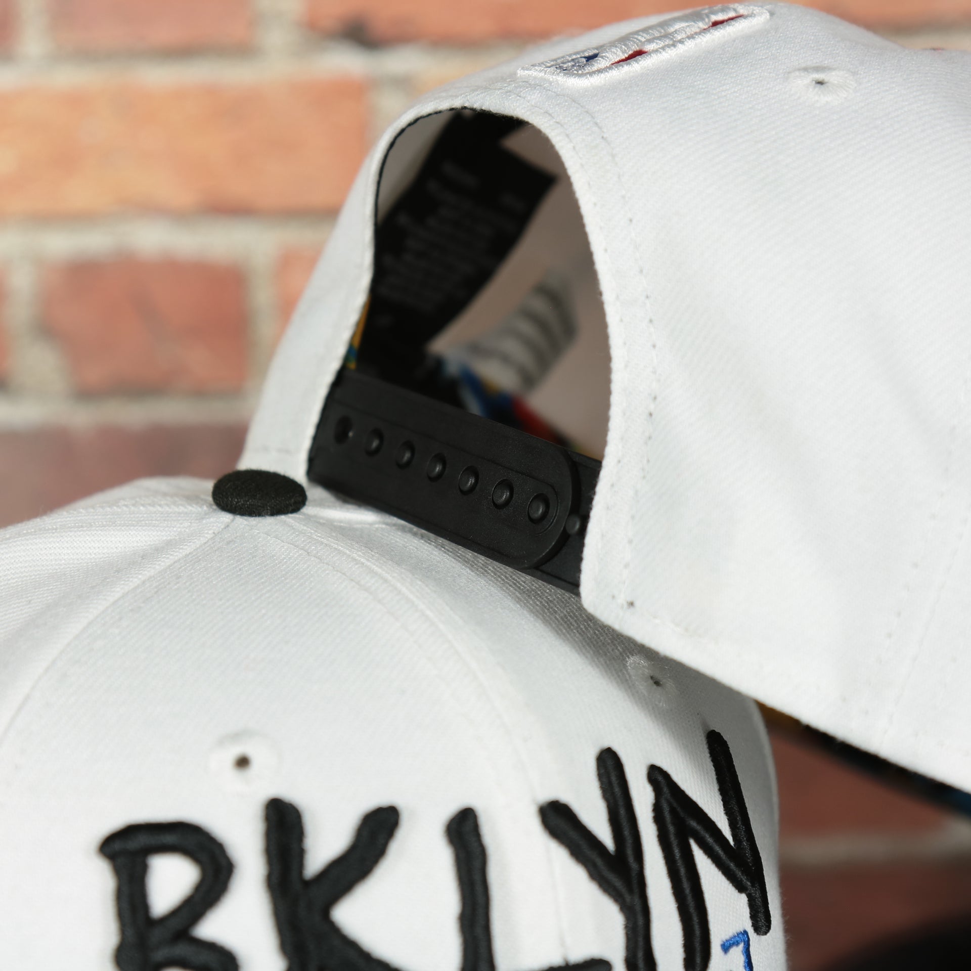 backside of the Brooklyn Nets 2022 City Edition BKLYN Nets Scribble Logo Multi-Color Bottom Youth 9Fifty Side Patch Snapback Cap | New Era, White