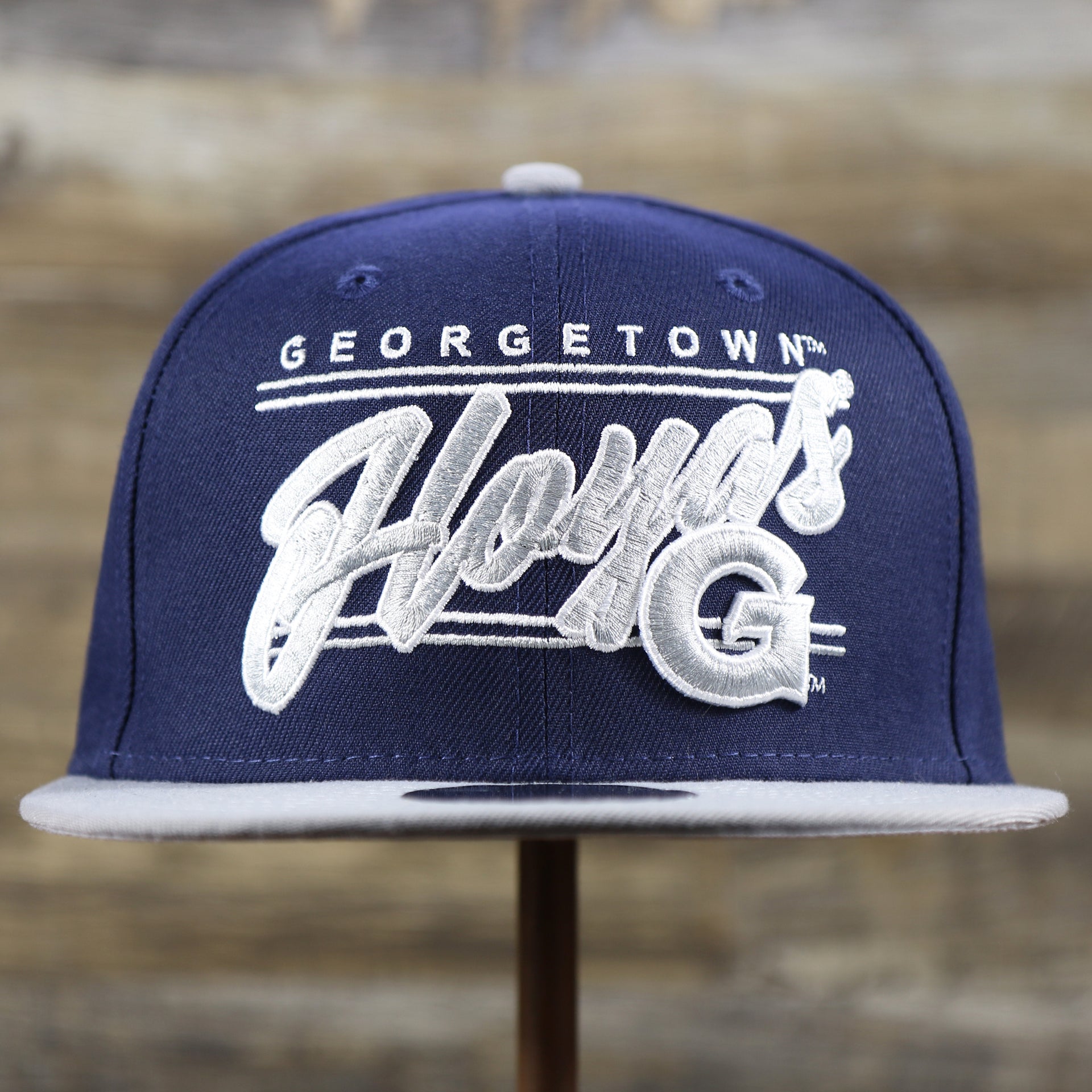 The front of the Georgetown Hoyas Team Script Gray Bottom 9Fifty Snapback | Navy Blue And Gray Snap Cap