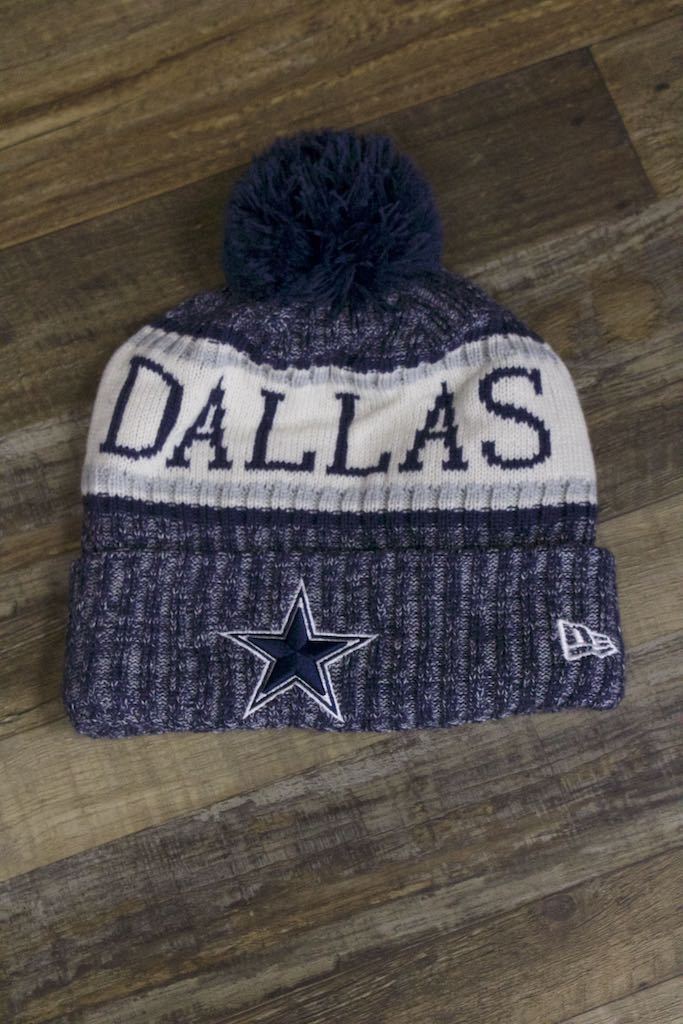 the Dallas Cowboys Winter Pom Beanie | 2018 On-Field Sideline Knit Cowboys Beanie has a dallas wordmark on the front and a big texas star logo