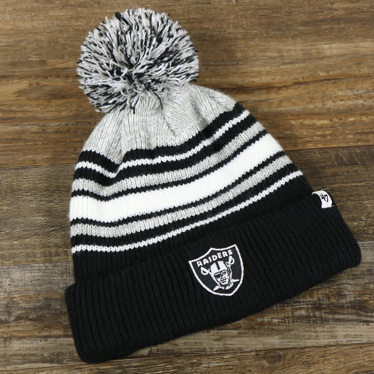 front side of the Kid’s Oakland Raiders Striped Cuffed Winter Beanie With Pom Pom | Kid’s  Black And Gray Winter Beanie