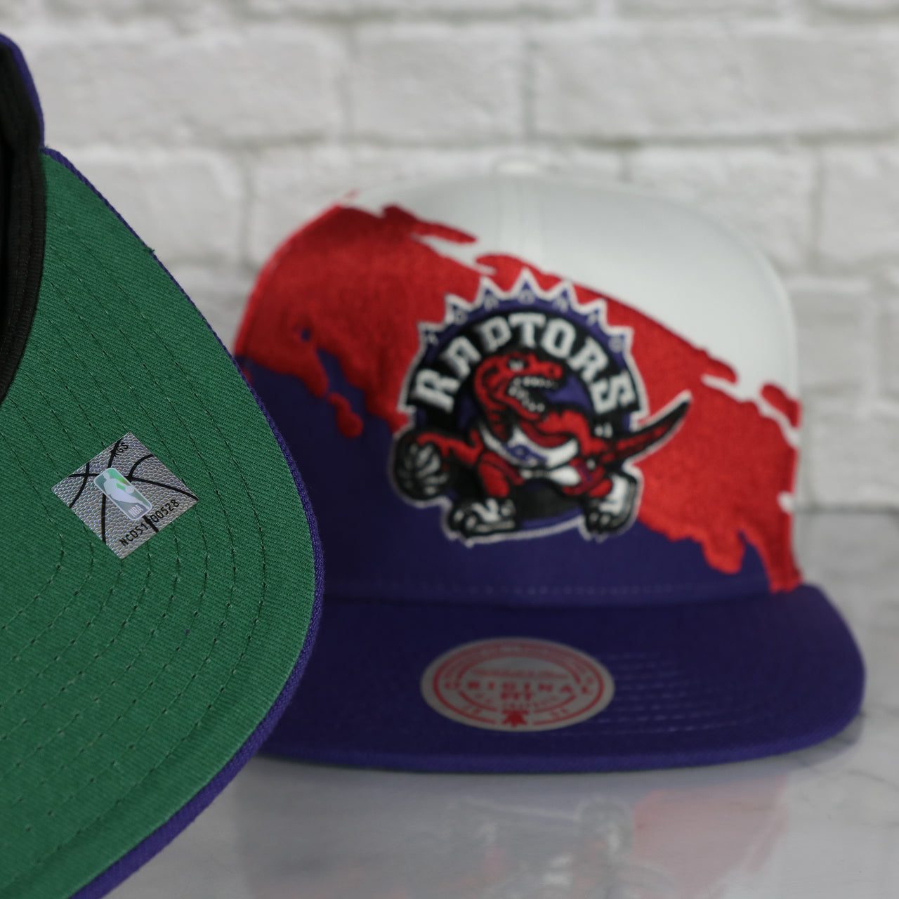green under visor on the Toronto Raptors Vintage Retro NBA Paintbrush Mitchell and Ness Snapback Hat | Purple/White/Red